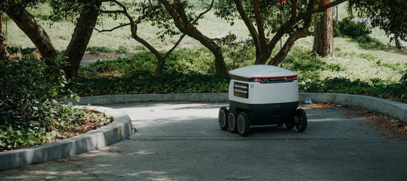 A sidewalk delivery robot driving down a footpath