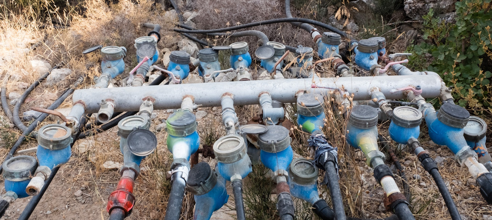 A photo of a large collection of various water valves and pipes, all connected to a white pipe. The assortment of valves and pipes appears fragile and cobbled together.