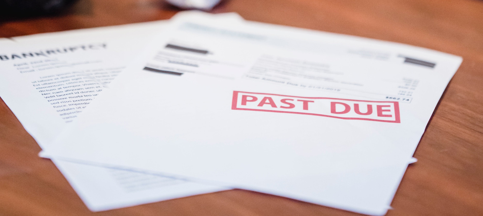 Photo of two sheets of paper on a table. The content of the paper is blurry but one has a readable heading bankruptcy and the other has a large red stamp "Past due".