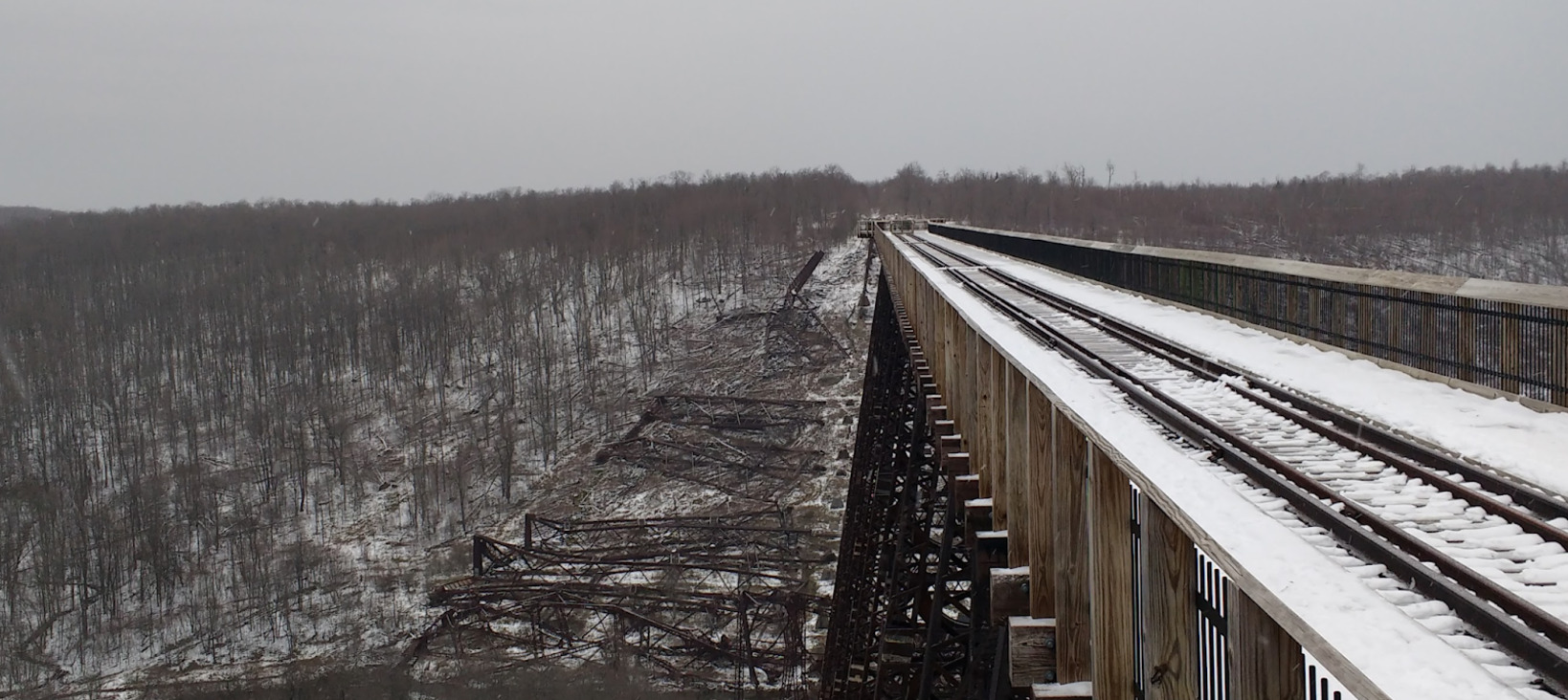 A photo of a bridge going into the distance over a valley in a winter landscape. About 50 meters ahead the bridge is collapsed with steel girders on the valley floor.