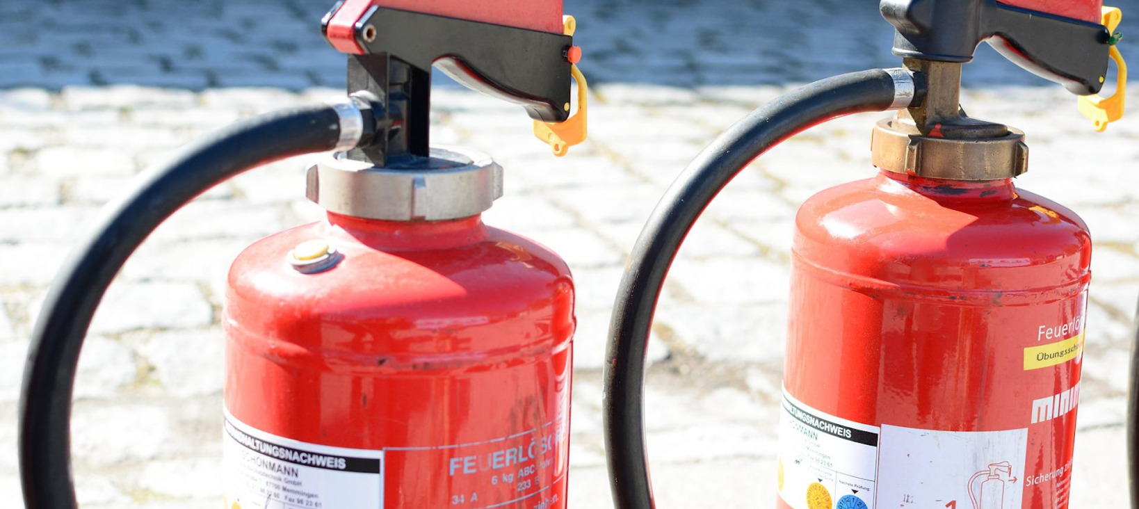 A photo of two fire extinguishers placed outside on the pavement in the sun.