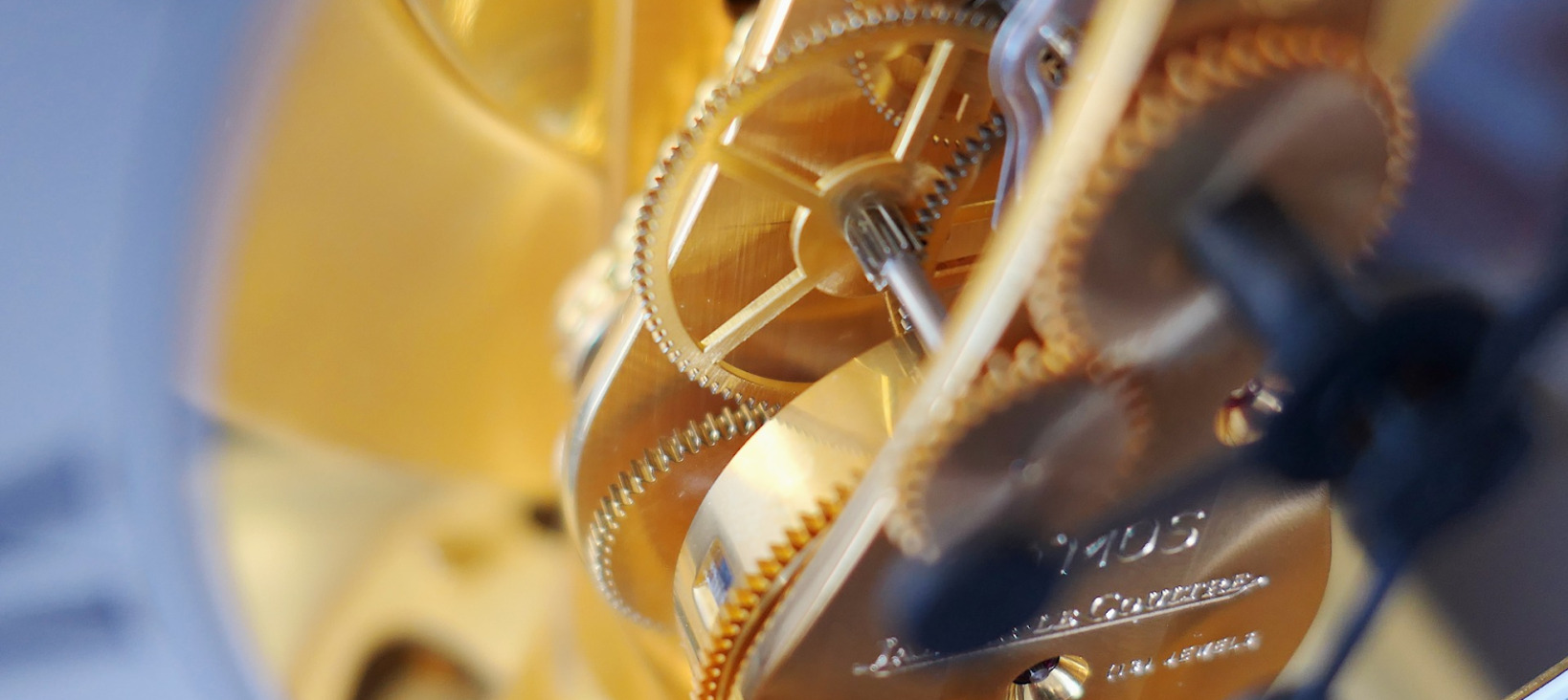 A close-up photo of the mechanics of a clock, showcasing its intricate details. The clock is made up of several gears appearing of fine texture and looking to have a golden color.